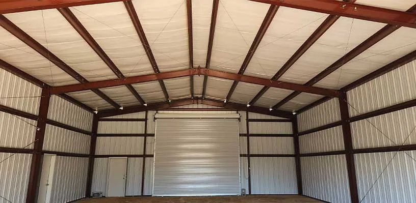 Large empty metal warehouse interior with high ceiling, steel walls, and closed roll-up door.