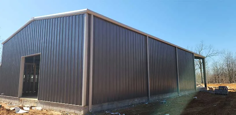Large metal-sided building on concrete blocks, surrounded by soil and construction materials.