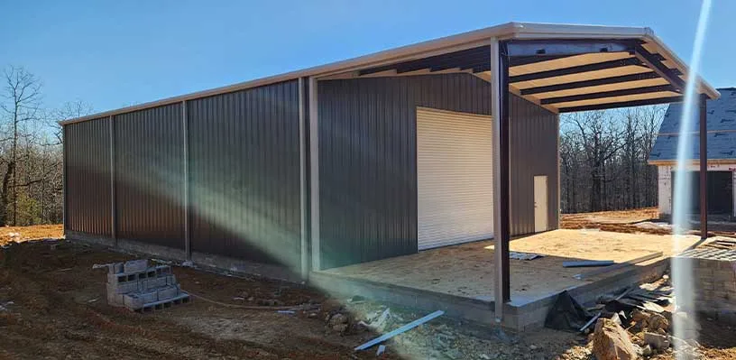 Metal structure under construction with open-sided area, white roll-up door, and nearby cinder blocks.