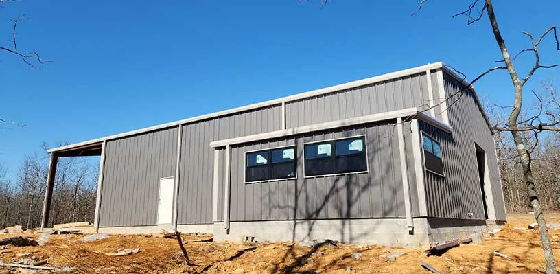 Modern metal building with slanted roof, windows, door, on rocky terrain under clear sky.