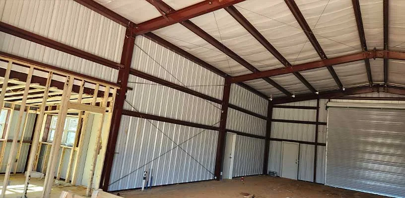 Partially constructed building interior with metal frame, roll-up door, and wooden wall framing.