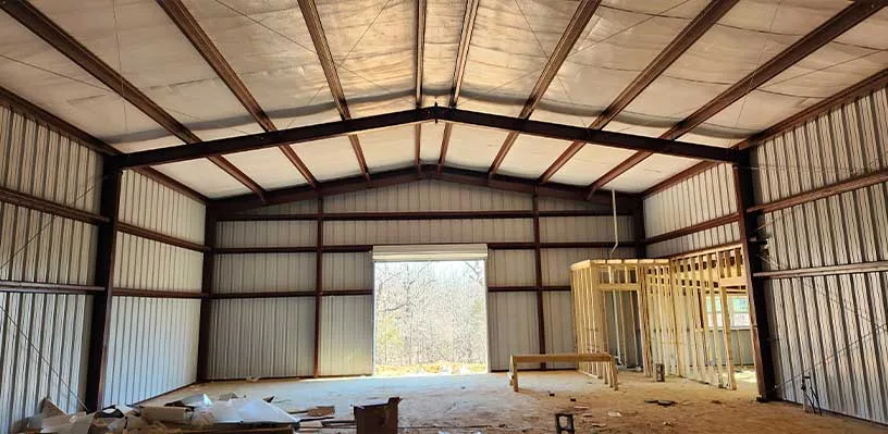 Unfinished metal building interior with wooden frame, exposed beams, corrugated walls, tools.